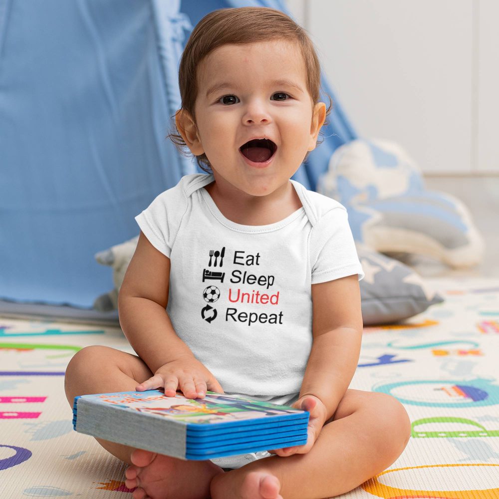 Happy baby boy sitting indoors in a white short-sleeve onesie featuring the phrase 