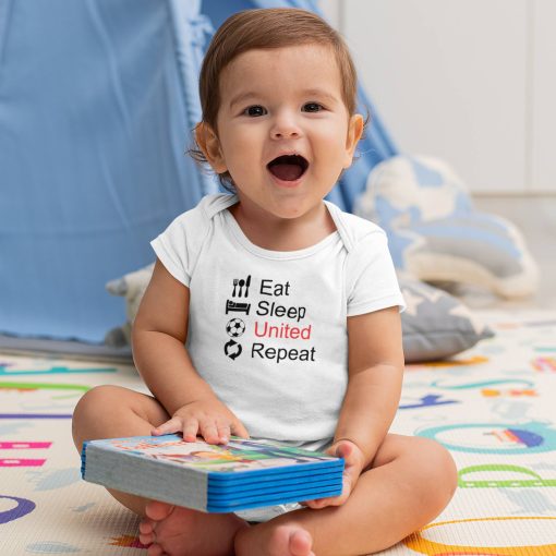 Eat Sleep United 09 Happy baby boy sitting indoors in a white short-sleeve onesie featuring the phrase "Eat Sleep United Repeat" with matching black icons and red “United” text, referencing Manchester United football club; playful soccer-themed baby apparel.
