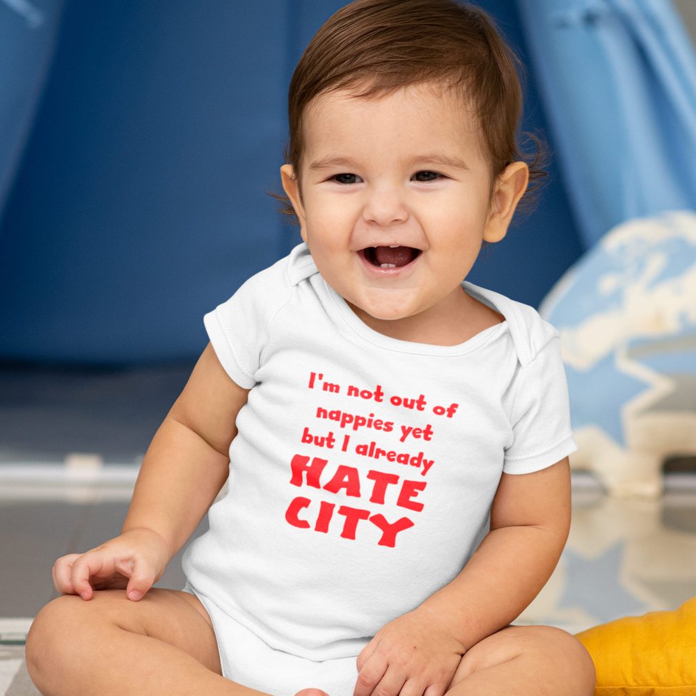 Laughing baby wearing a white onesie with bold red text that reads, 