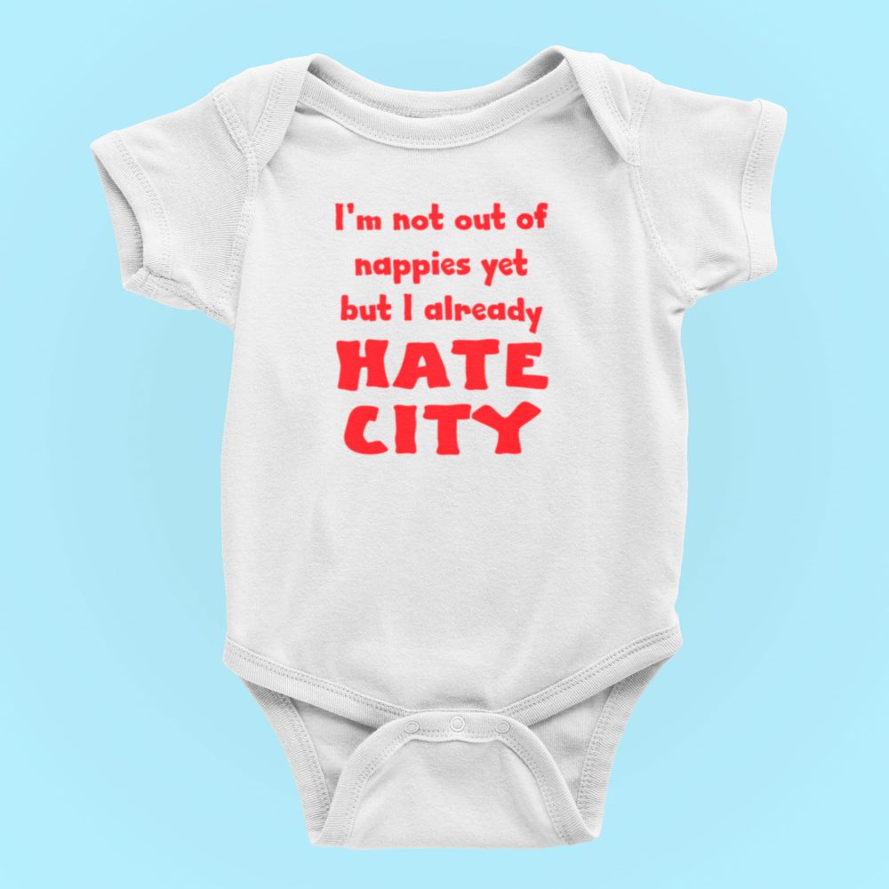 Image Alt Text Generator said: White baby onesie displayed on a light blue background, featuring bold red text that reads, "I'm not out of nappies yet but I already HATE CITY." The humorous football-themed design targets fans of rival teams opposed to Manchester City FC, making this item ideal for sports baby clothes, soccer rivalry merchandise, and gift ideas for football fan parents. Optimized for keywords like “anti-Man City baby onesie,” “funny football baby bodysuit,” and “soccer fan infant apparel.”