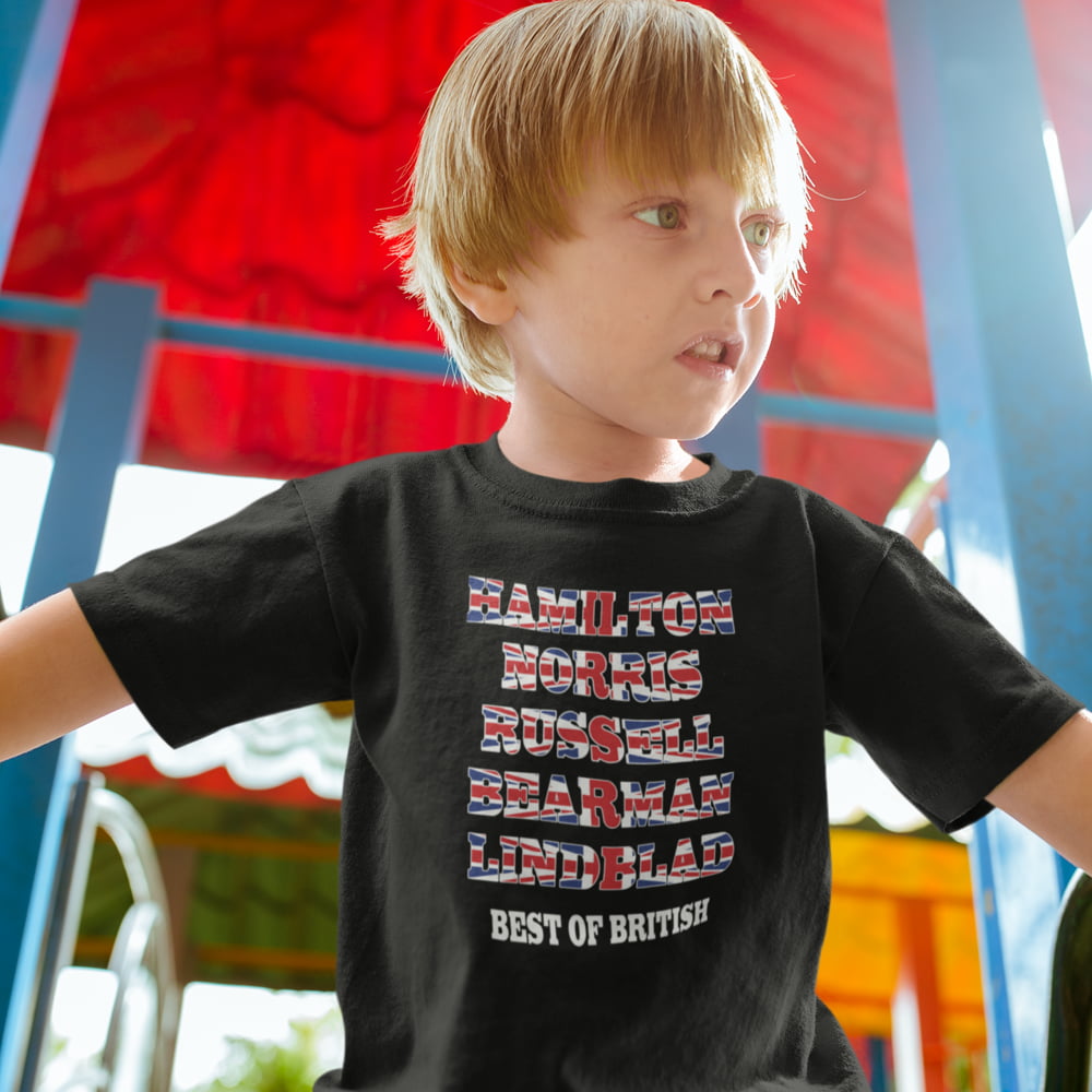 Smiling child outdoors wearing a black kids Formula One T-shirt with a Union Jack-style text design featuring Hamilton, Norris, Russell, Bearman and Lindblad, with “Best of British” printed underneath.